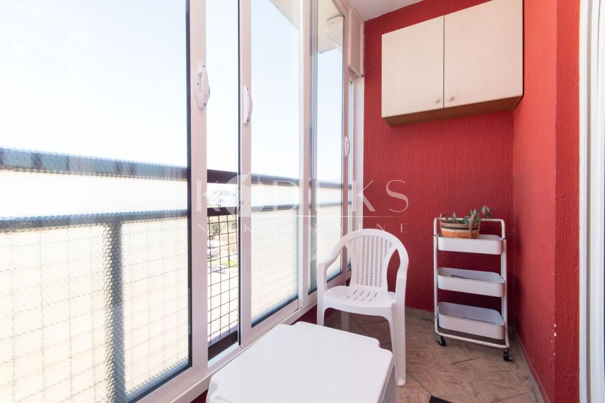 Zastakljeni balkon sa stocem, stolicom i policom na crvenom zidu.