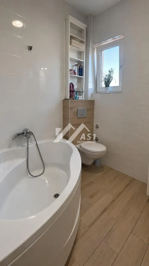 Modern bathroom with a bathtub, toilet and built-in shelves.