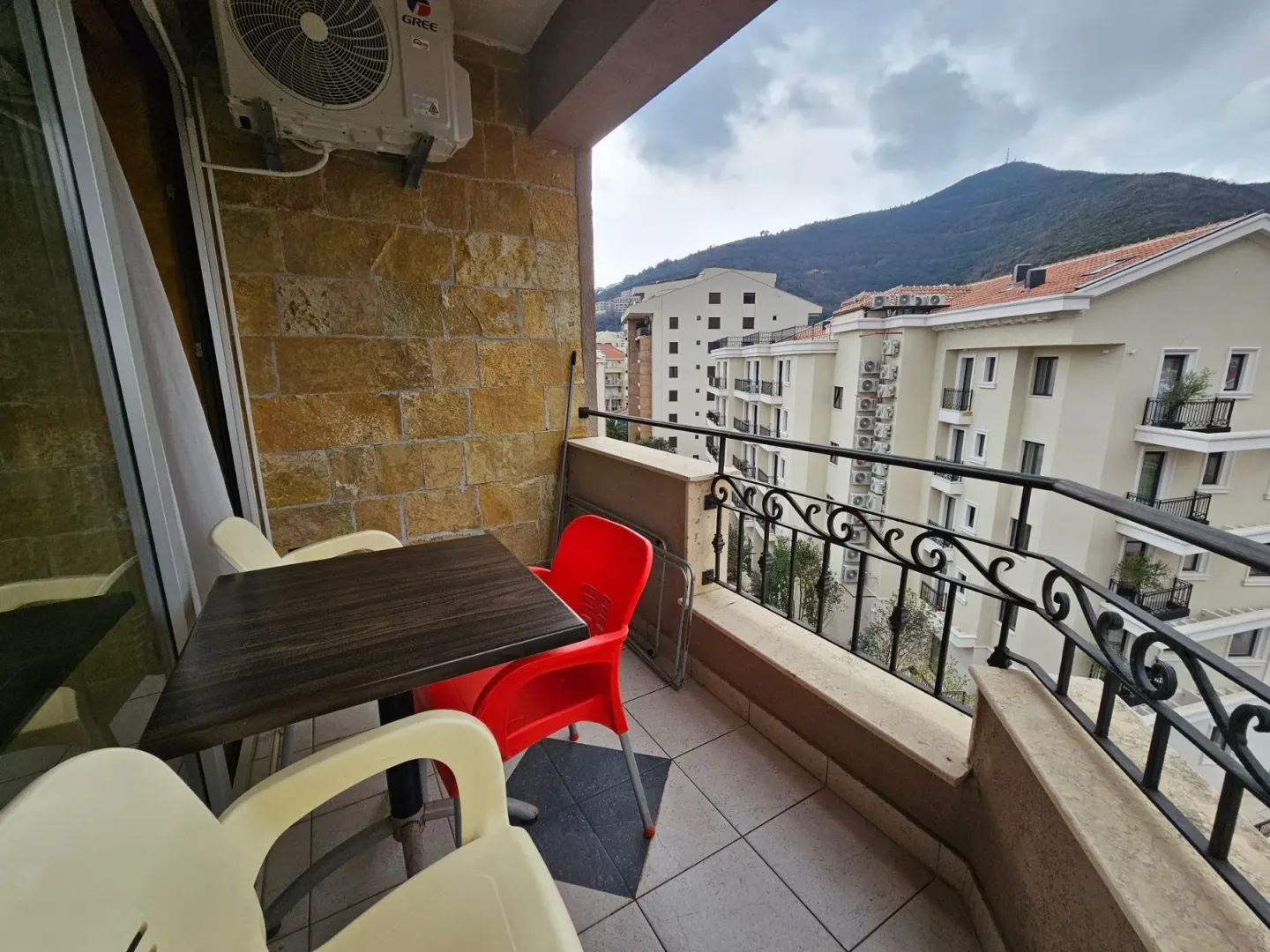 Furnished balcony with a table, chairs, and a view of surrounding buildings and hills.