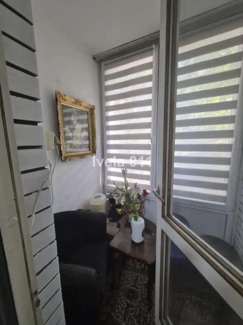 Zastakljeni balkon sa malom foteljom i stočićem.