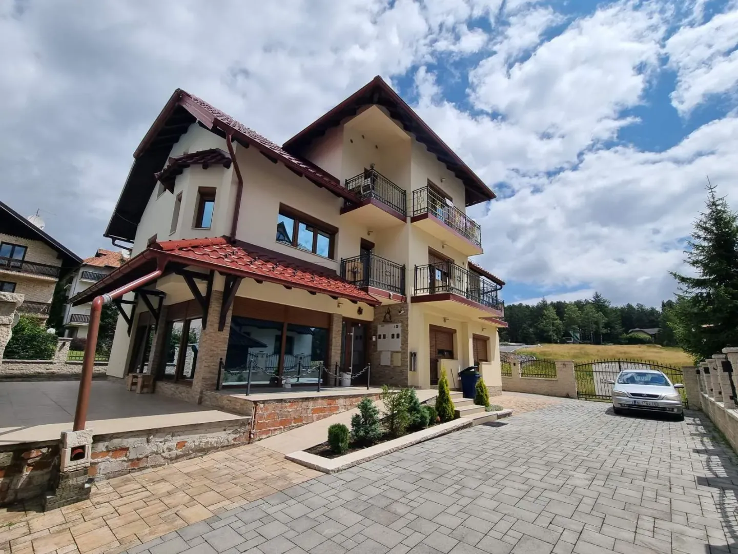 Eksterijer višespratne kuće sa dvorištem i popločanim prilazom.