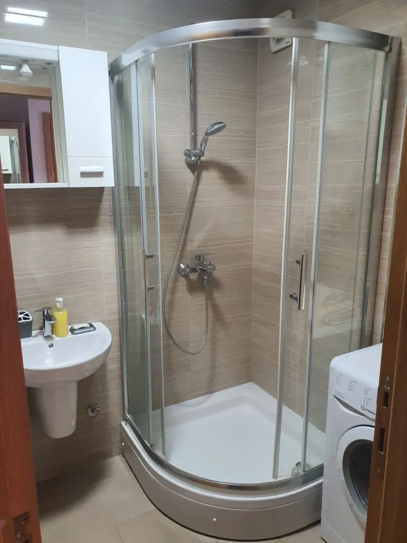Small bathroom with a shower cabin, washbasin, and washing machine.