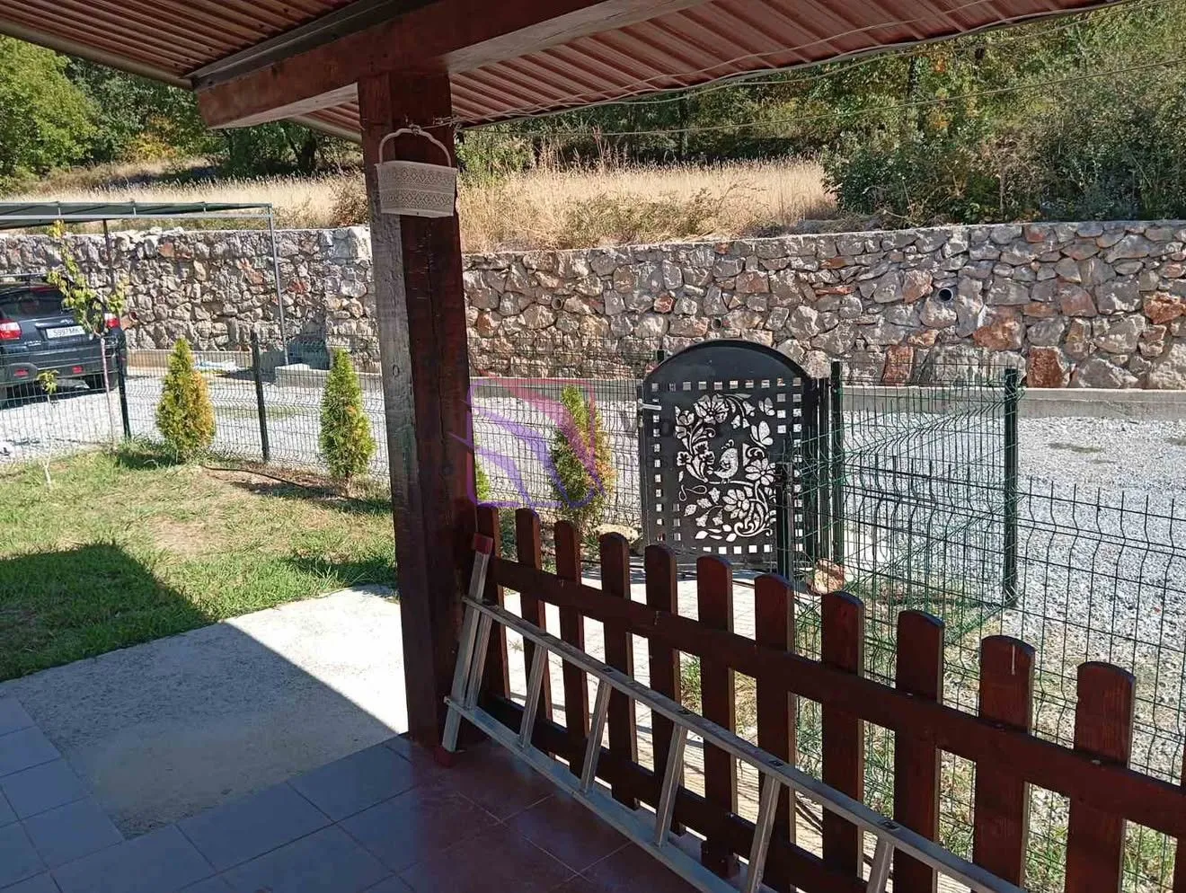 View from the covered terrace to the yard and gate with a stone wall.