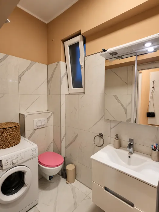 Kupatilo opremljeno umivaonikom, WC šoljom, mašinom za veš i ogledalom sa rasvetom.