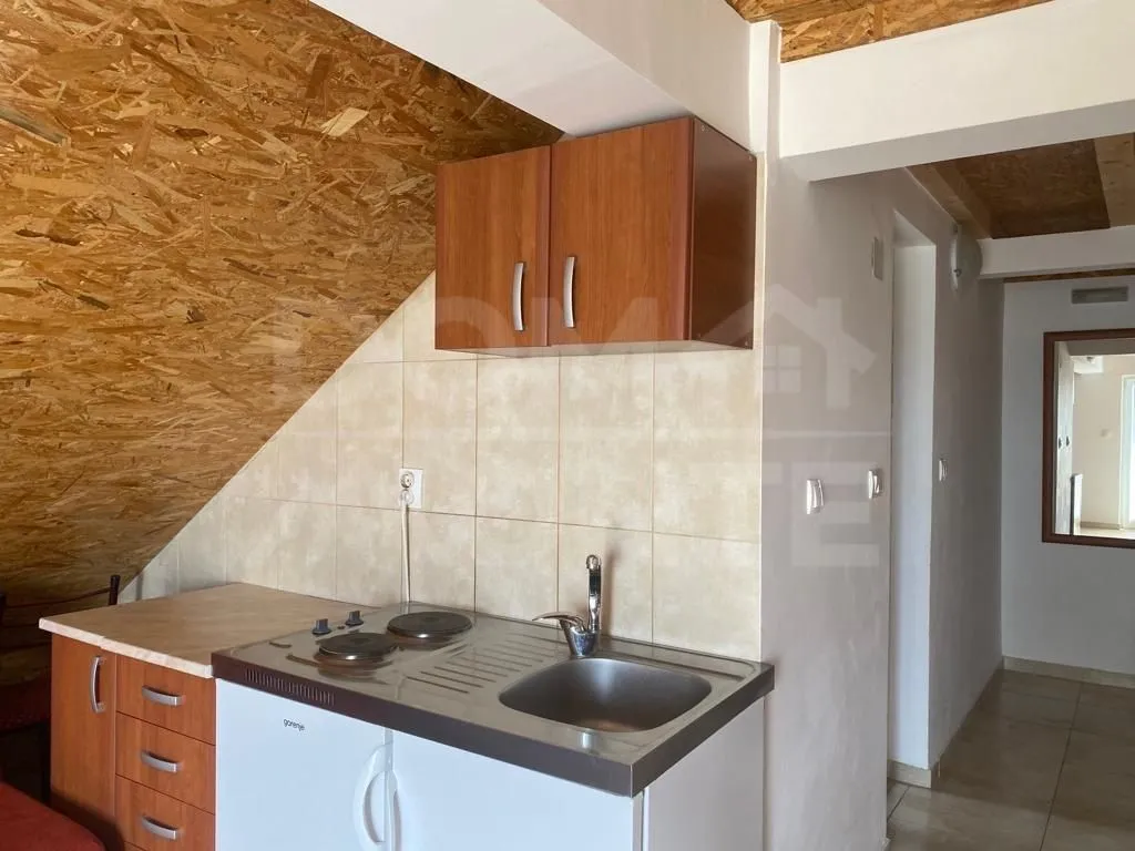 Small kitchen with a sink, stove, and wooden cabinetry in the attic.