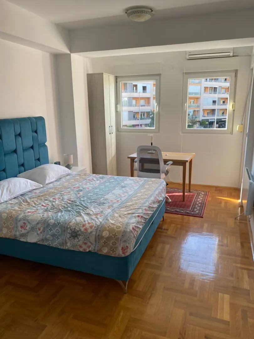 Spavaća soba sa bračnim krevetom, radnim stolom i prozorima.