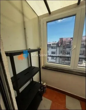 Enclosed balcony with a shelving unit and view of surrounding buildings. - image 9