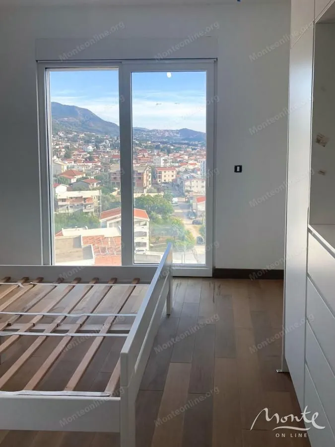 Spavaća soba sa krevetom i velikim prozorom sa pogledom na grad.