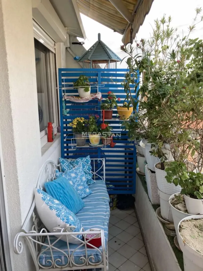 Namešten balkon sa klupom, jastucima i saksijama sa cvećem.