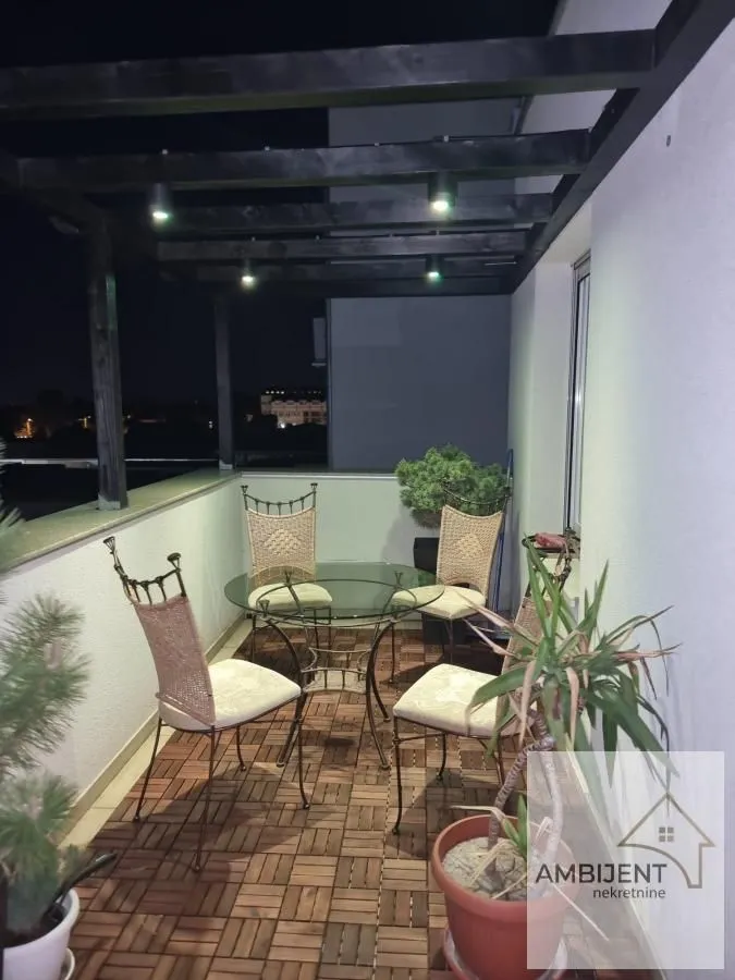 Nameštena terasa sa garniturom za sedenje i drvenom pergolom noću.