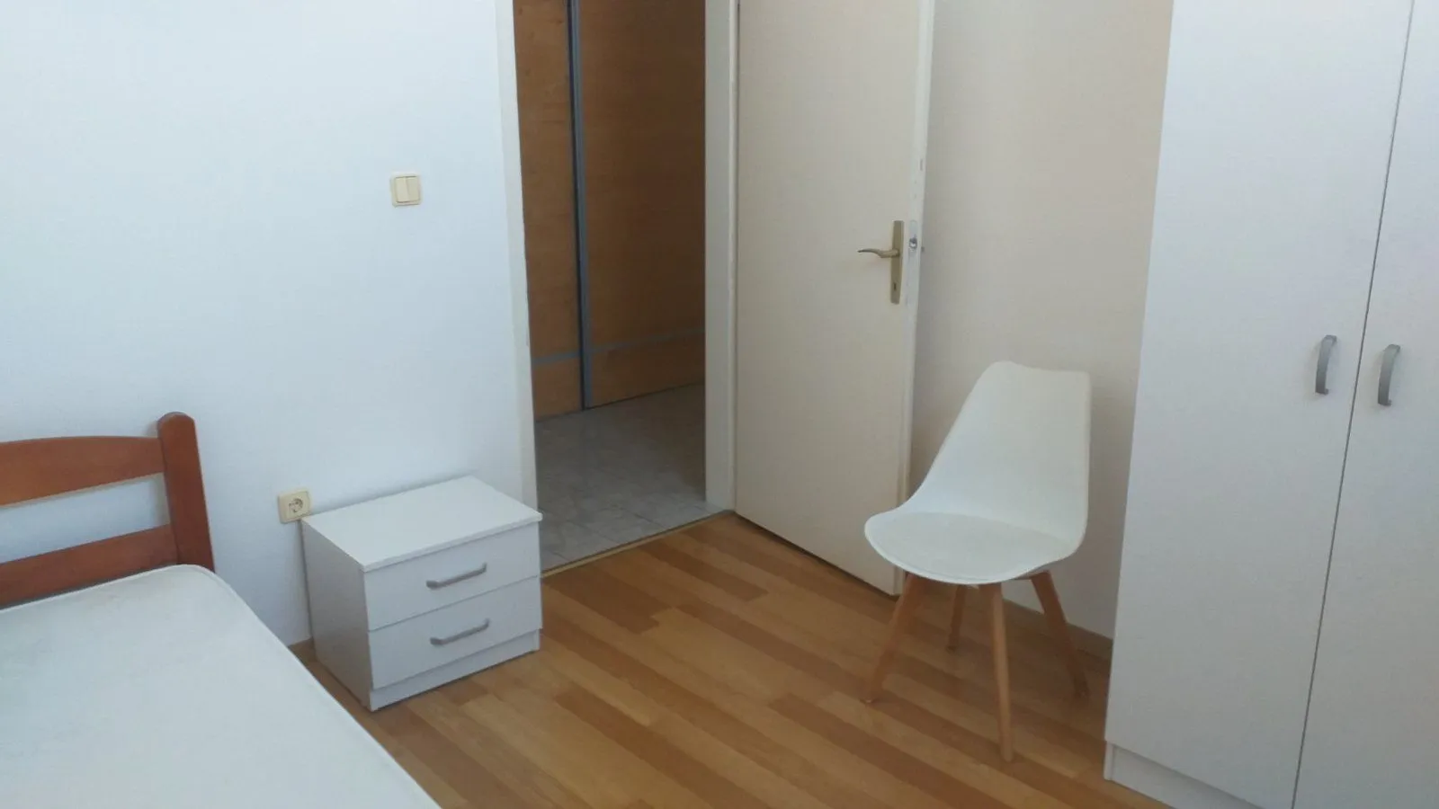 Jednostavna spavaća soba sa bijelim namještajem i drvenim podom.