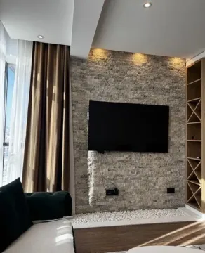 Living room with a stone feature wall and a television. - image 2