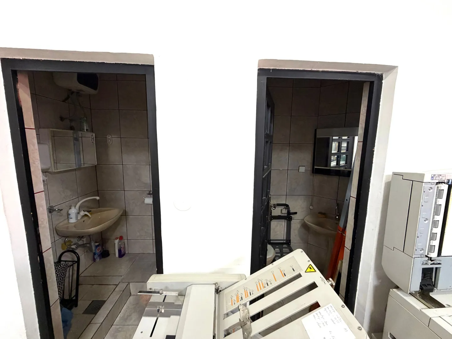 View of two bathrooms from a hallway with office equipment.