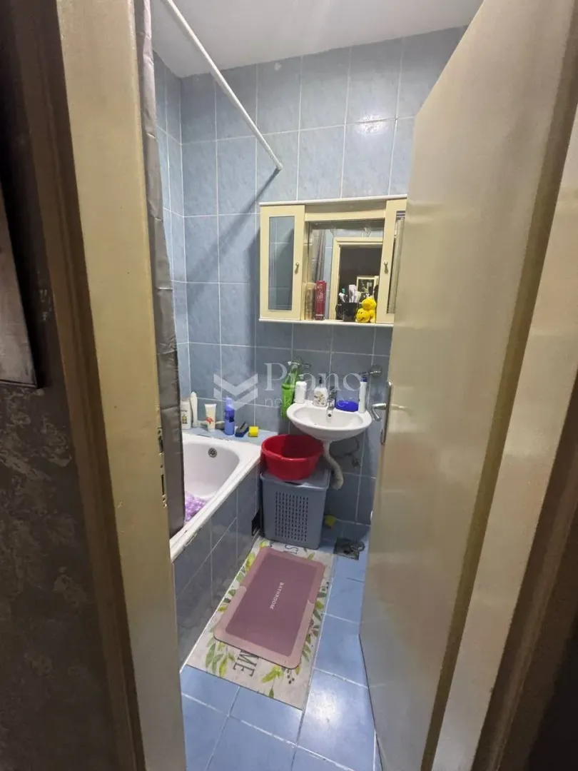 Manje kupatilo sa kadom, umivaonikom i zidnim ormarićem.