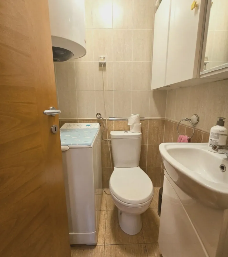 Manje kupatilo sa WC šoljom, umivaonikom i veš mašinom.