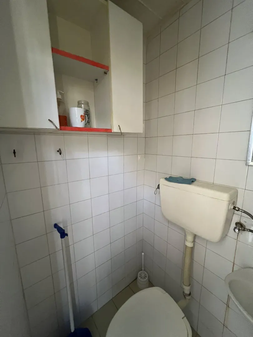 A simple toilet with white tiles and a wall cabinet.