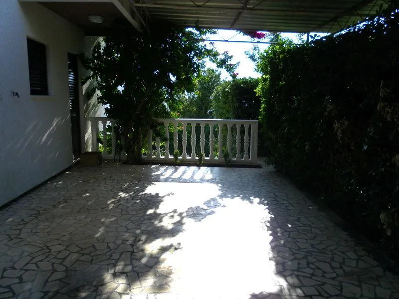 Prostrana popločana terasa sa ogradom i zelenilom.