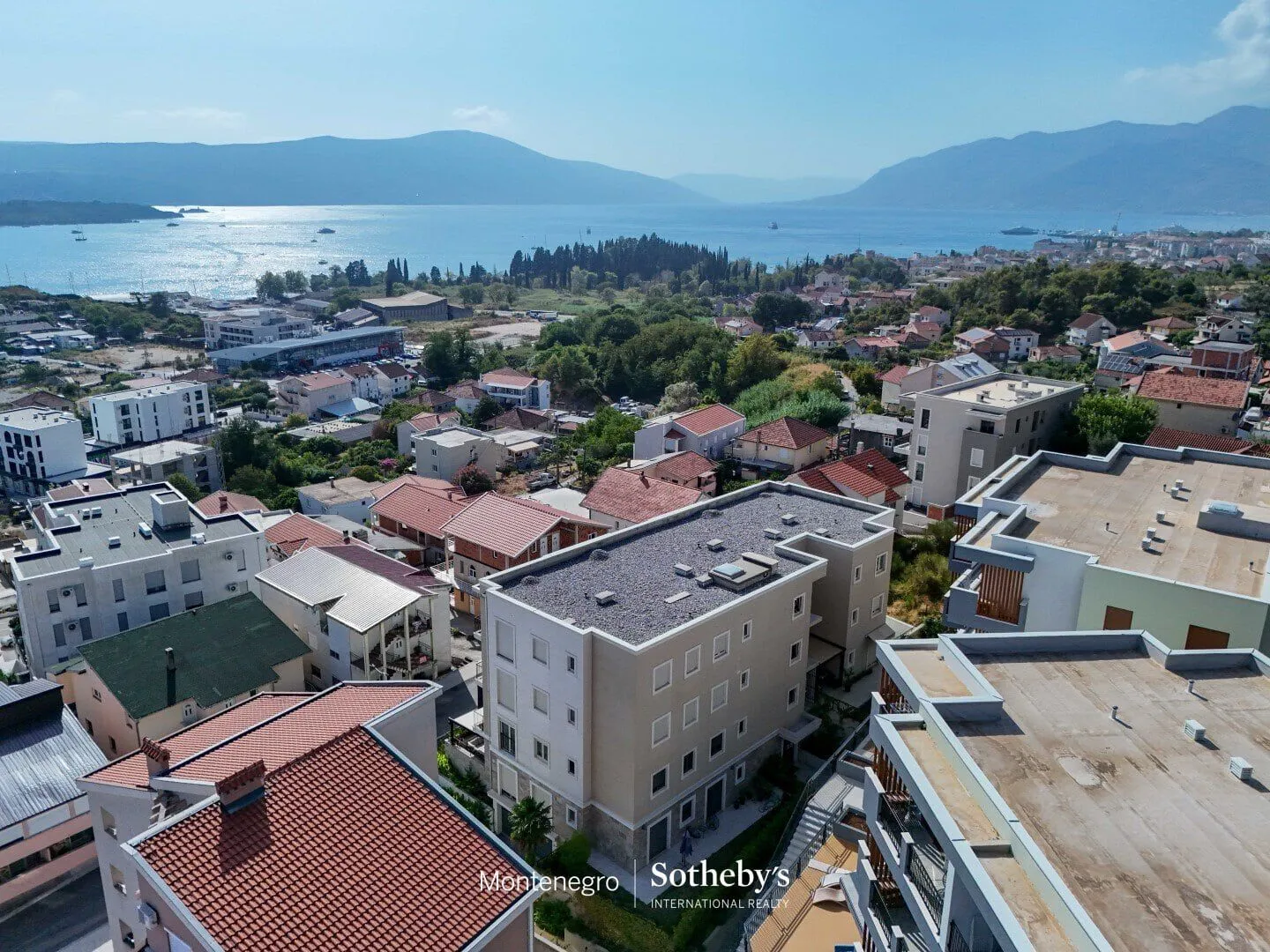 Pogled iz vazduha na zgradu i okolno naselje sa pogledom na more.