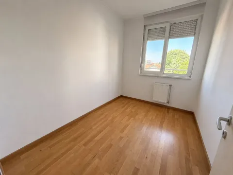 Prazna soba sa belim zidovima, drvenim parketom i prozorom. - image 10