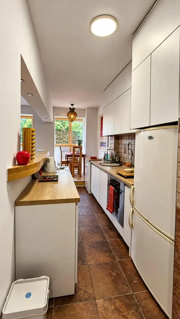 Long kitchen with white cabinets and a dining area in the background.