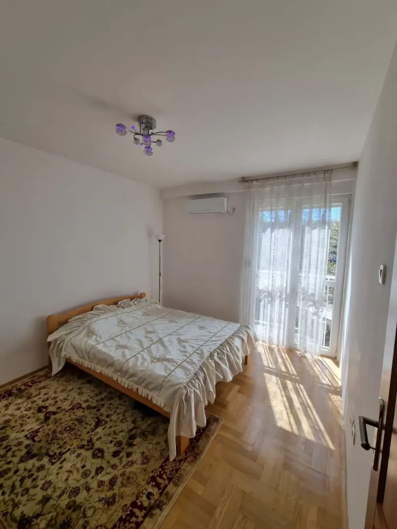 Svijetla spavaća soba sa bračnim krevetom i izlazom na balkon.