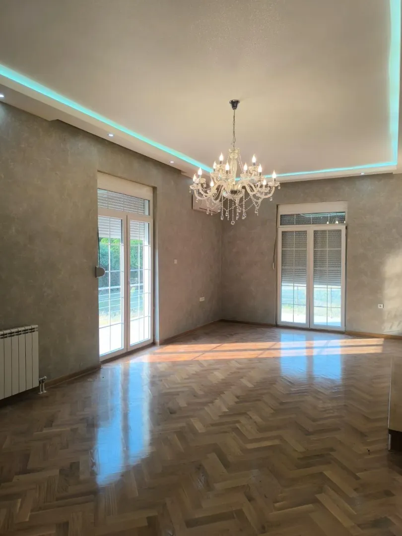 Spacious empty room with parquet flooring, a chandelier, and two balcony doors.