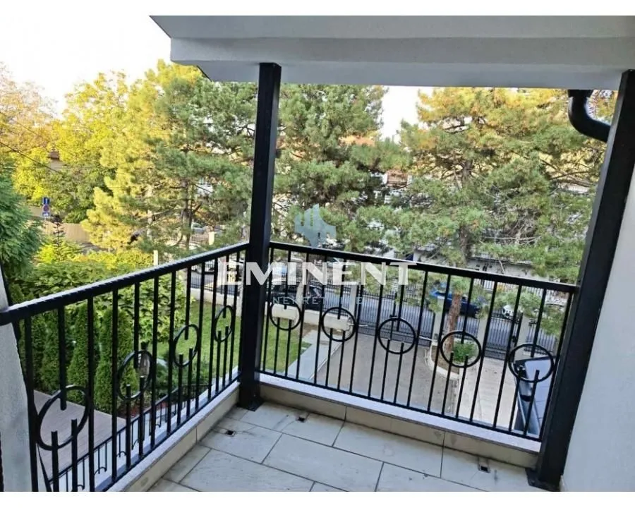 Natkriveni balkon sa crnom ogradom i pogledom na zelenilo i ulicu.