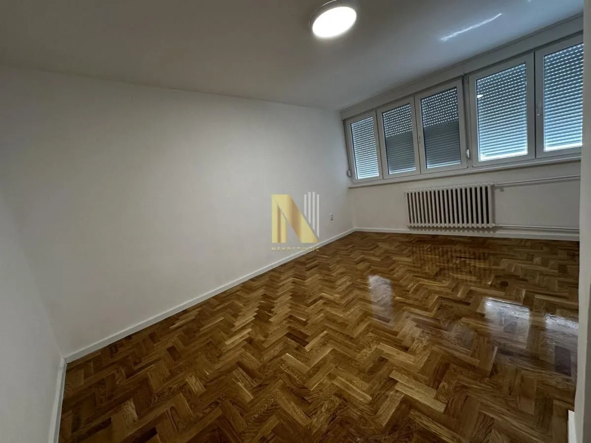 Prazna soba sa parketom i velikim prozorima.