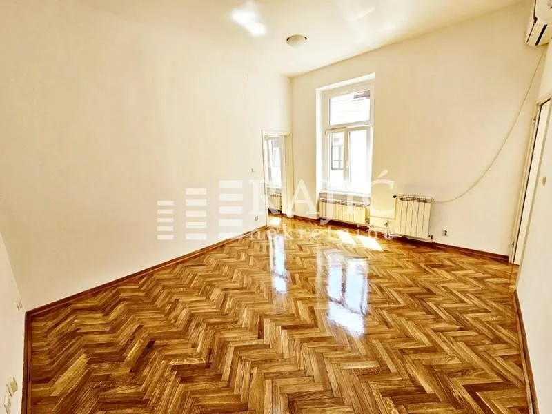 Empty room with parquet flooring and a large window.