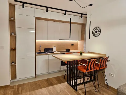 Moderna kuhinja sa drvenim elementima, ugradnim aparatima i trpezarijskim stolom sa narandžastim stolicama. - image 7