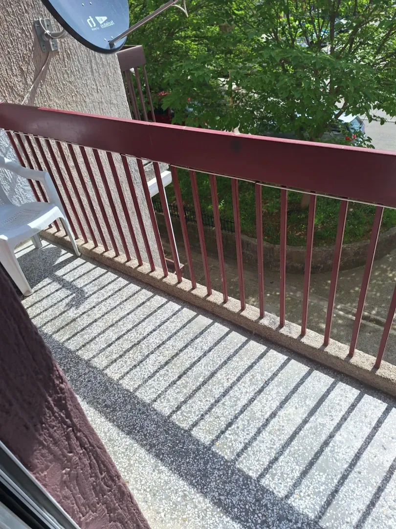 Small balcony with metal railing and green view.