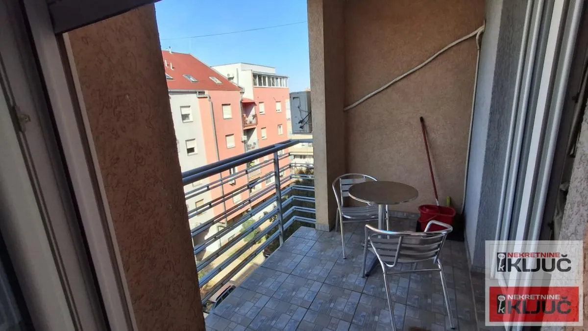 Natkriveni balkon sa garniturom za sedenje i metalnom ogradom.