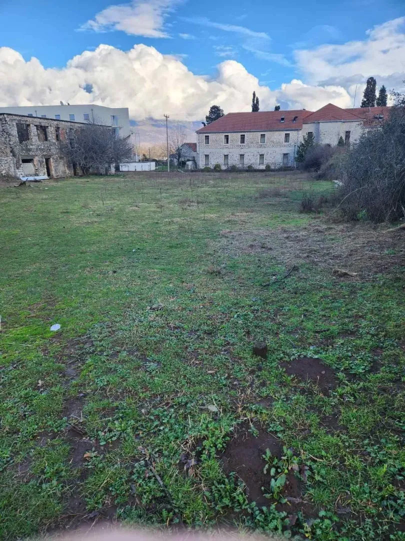 Prostrani travnati plac okružen kamenim kućama pod plavim nebom.