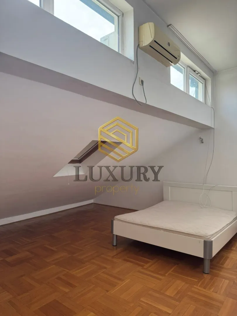 Attic bedroom with a white bed and parquet flooring.