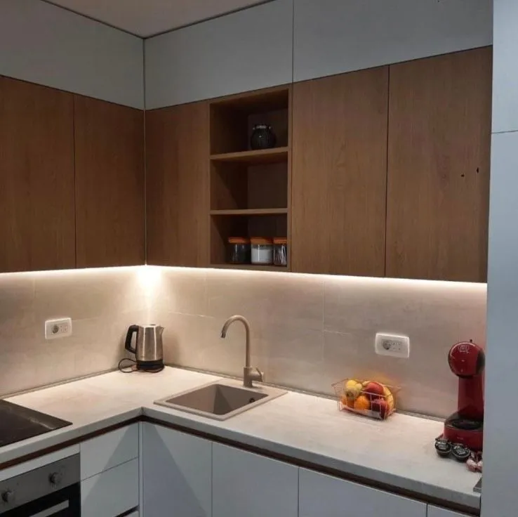 Modern kitchen with white lower cabinets, wooden upper cabinets, and integrated lighting.