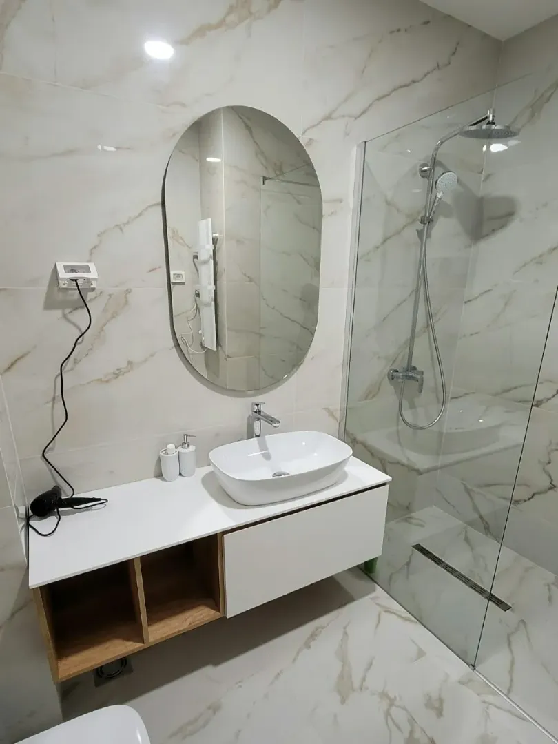 Moderne kupatilo sa umivaonikom, ogledalom i tuš kabinom.