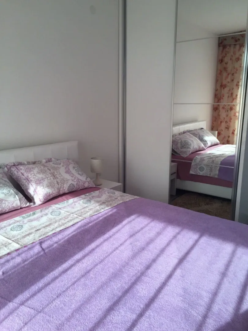 Svijetla spavaća soba sa velikim bračnim krevetom i ugradnim plakarom sa ogledalom.
