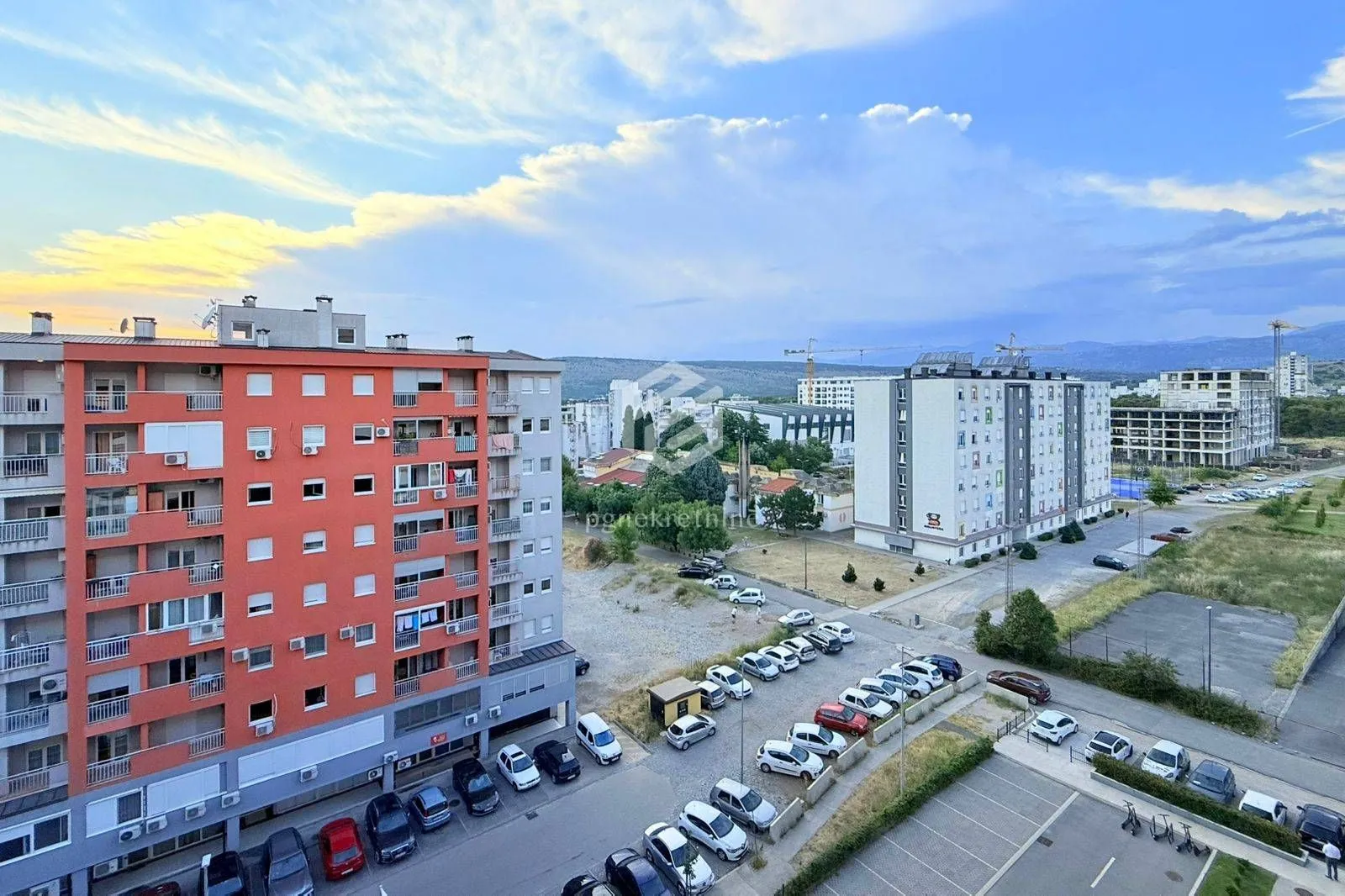 Pogled sa prozora na okolne zgrade, parking i gradski pejzaž.
