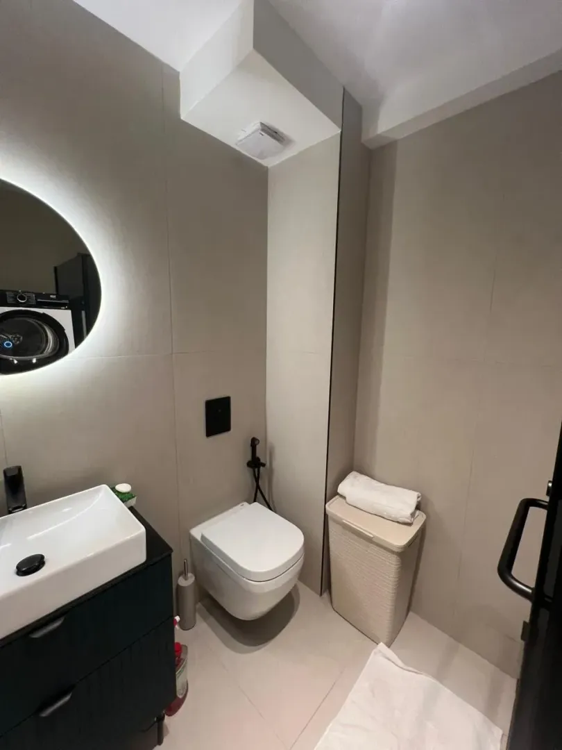 Modernly equipped bathroom with a washbasin, toilet, and backlit mirror.