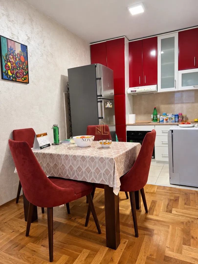 Trpezarija sa stolom i crvenim stolicama pored kuhinje.