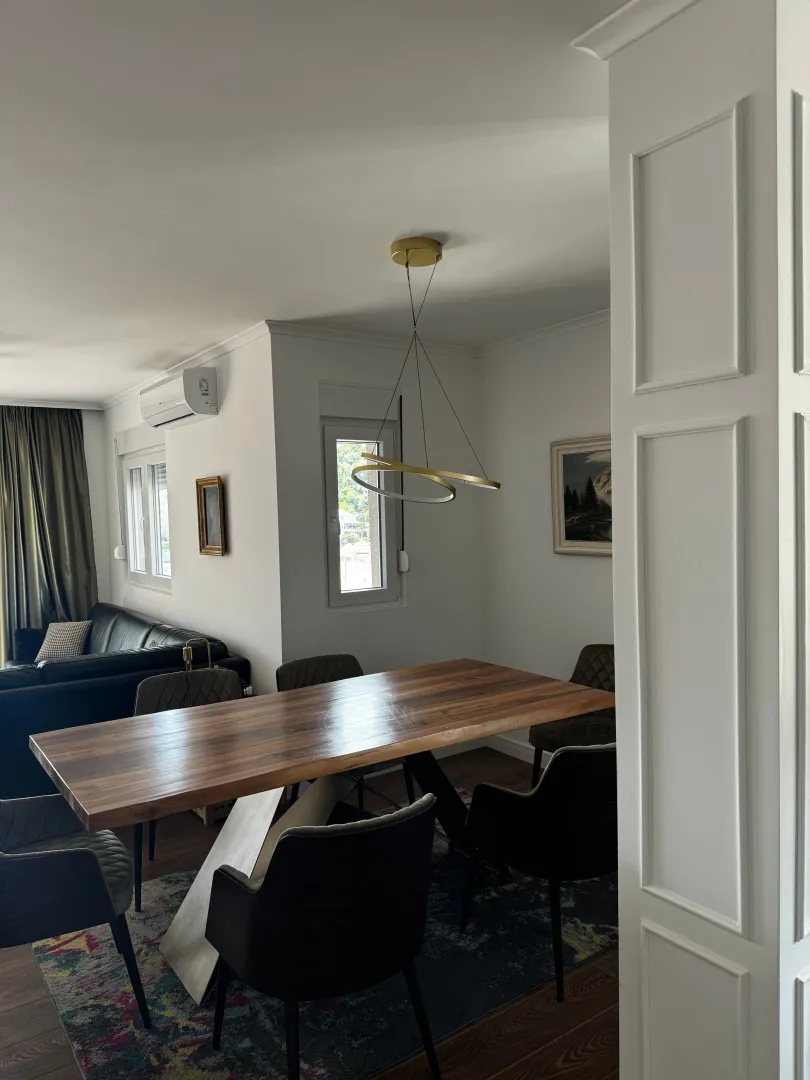 Trpezarija sa velikim drvenim stolom i modernim lusterom.