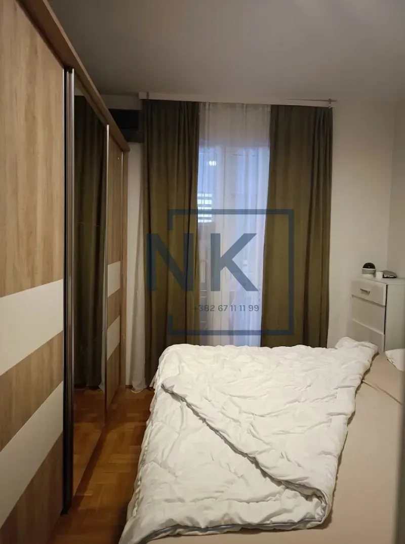 Spavaća soba sa bračnim krevetom, velikim ormarom i prozorom sa zavesama.