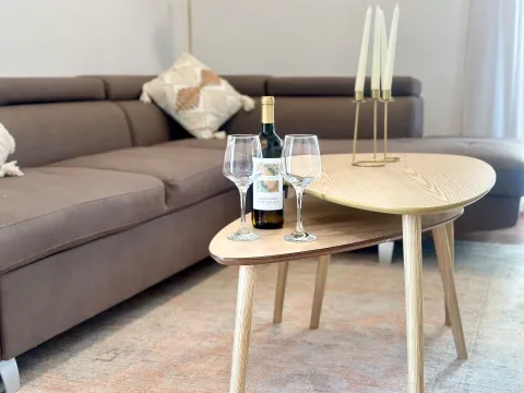 Dnevna soba sa braon ugaonom garniturom i drvenim stočićem sa flašom vina i čašama. - image 4