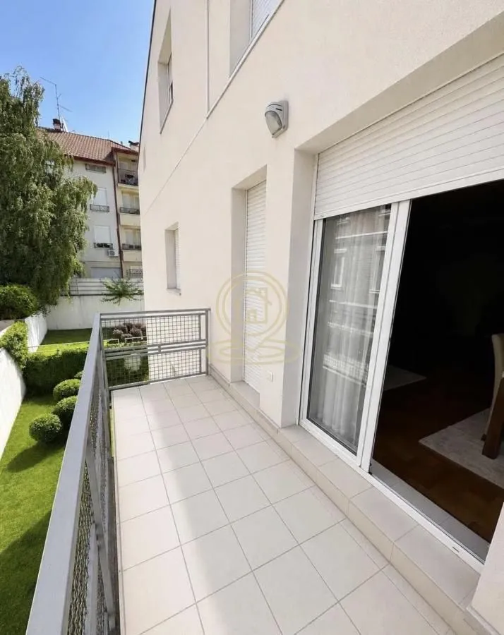 Prostrani popločani balkon sa metalnom ogradom i pogledom na dvorište.