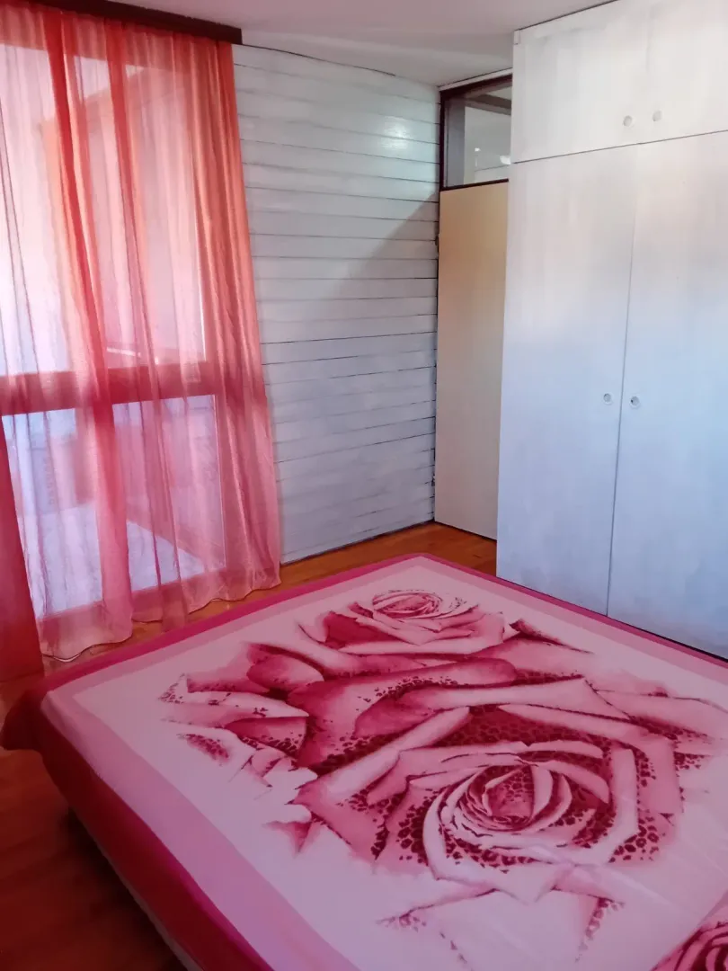 Spavaća soba sa velikim bijelim plakarom i krevetom sa ružičastim prekrivačem.