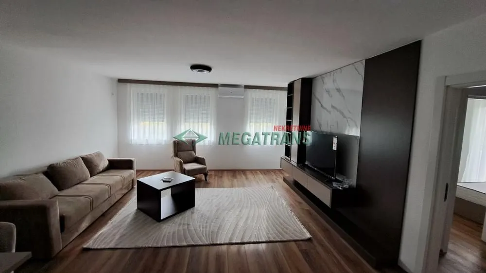 Prostrani dnevni boravak sa garniturom za sedenje i TV komodom.