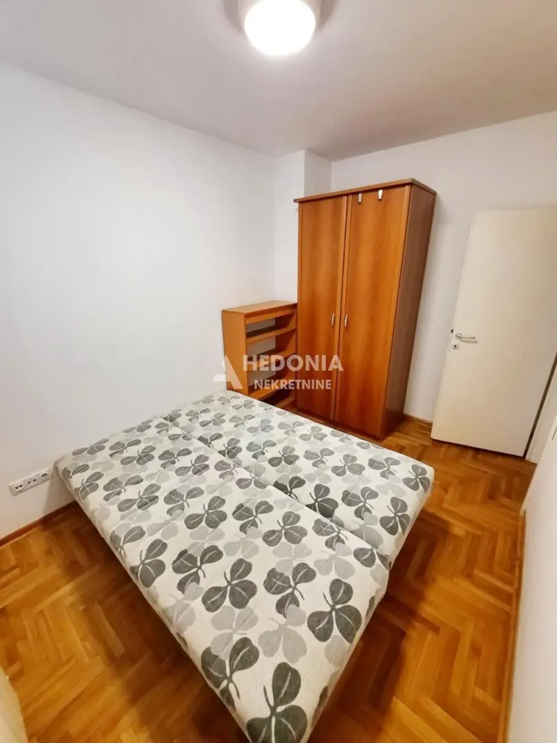 Furnished bedroom with a double bed, wooden wardrobe, and parquet flooring.