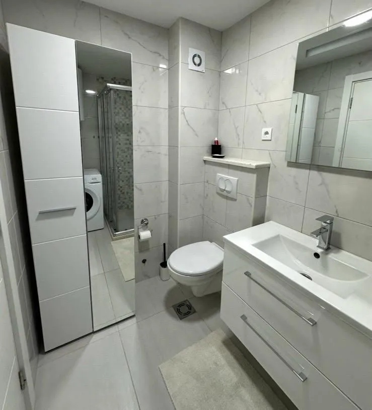 Modern bathroom with white furniture, a walk-in shower, and a washing machine.