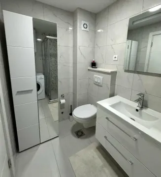 Modern bathroom with white furniture, a walk-in shower, and a washing machine. - image 8