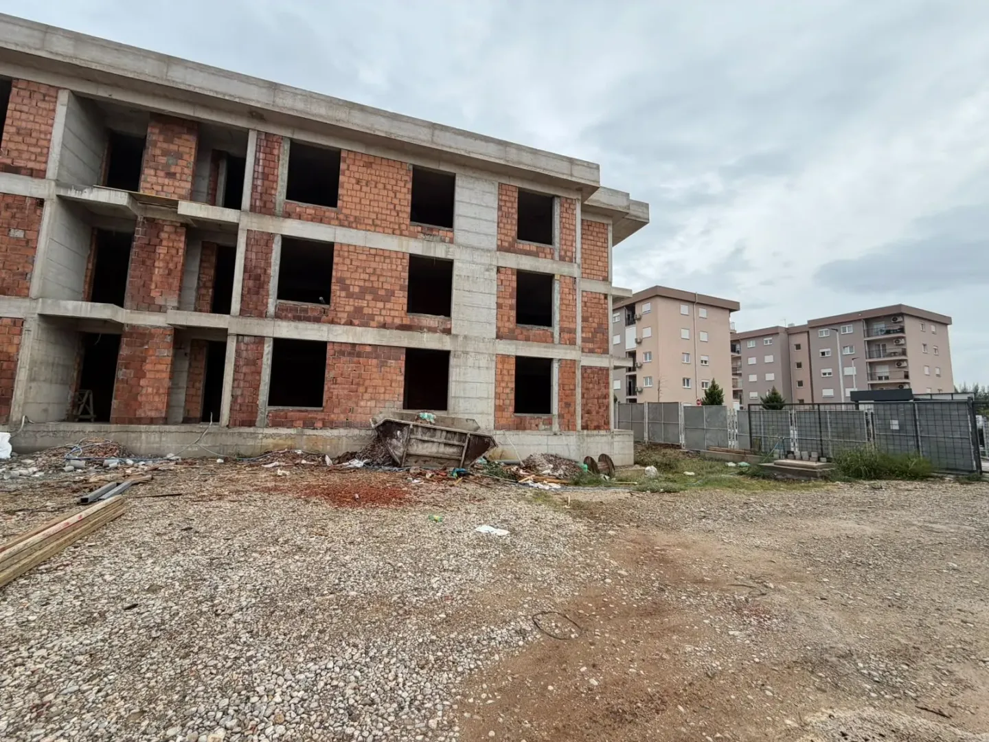 Spoljašnjost zgrade u izgradnji sa nedovršenom fasadom i okolnim dvorištem.